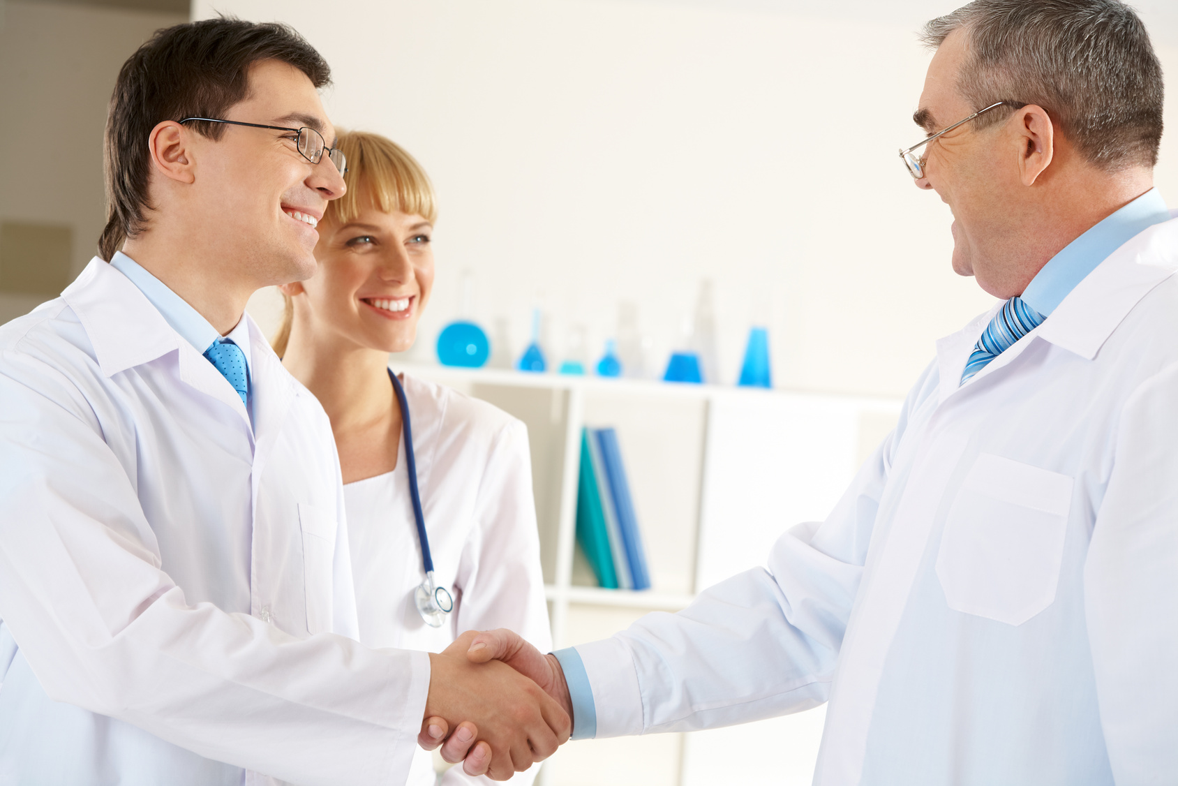 Photo of aged physician and young clinician handshaking with friendly nurse near by